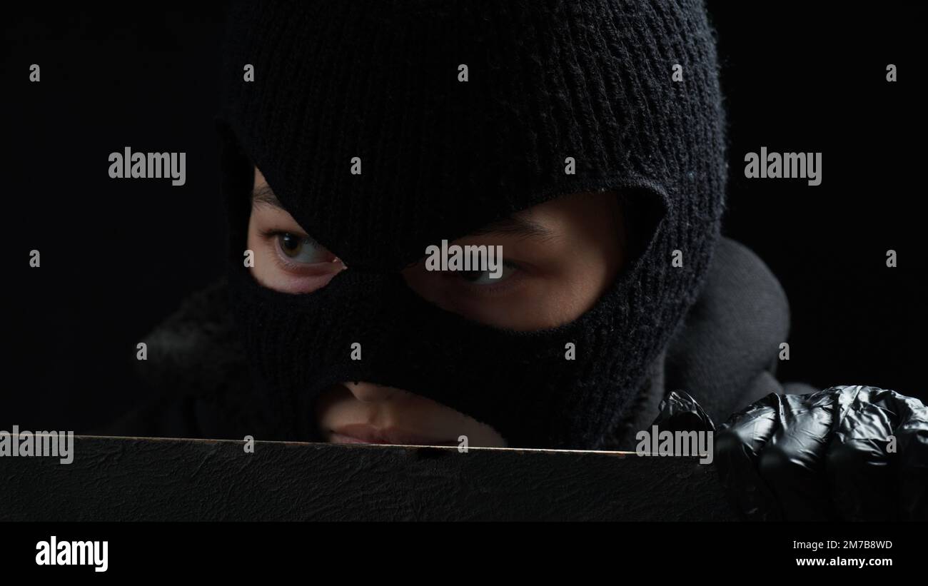 Une femme masquée cambrioleur en gants noirs regarde au-dessus d'une clôture. Concept de crime Banque D'Images