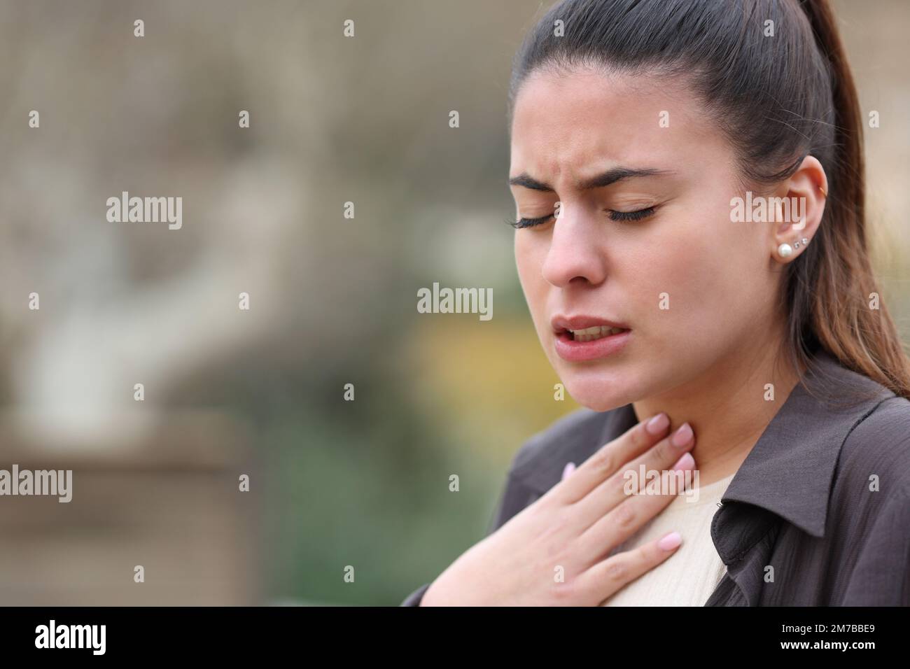 Femme se plaignant de mal de gorge dans un parc Banque D'Images