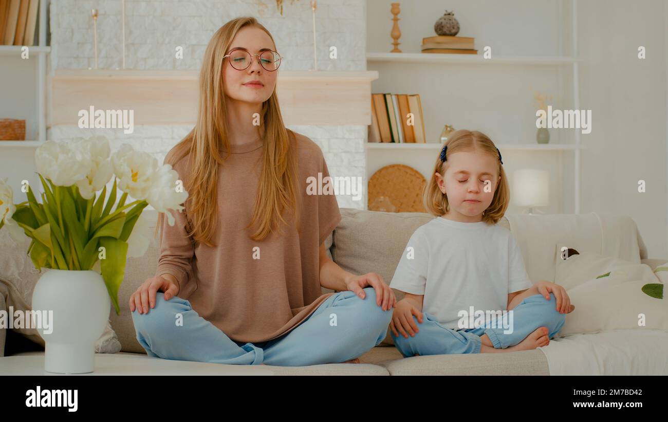 Femme caucasienne maman avec petite fille assise à la maison au canapé en position de lotus yeux fermés méditer ensemble. La famille méditant la mère enseigner Banque D'Images