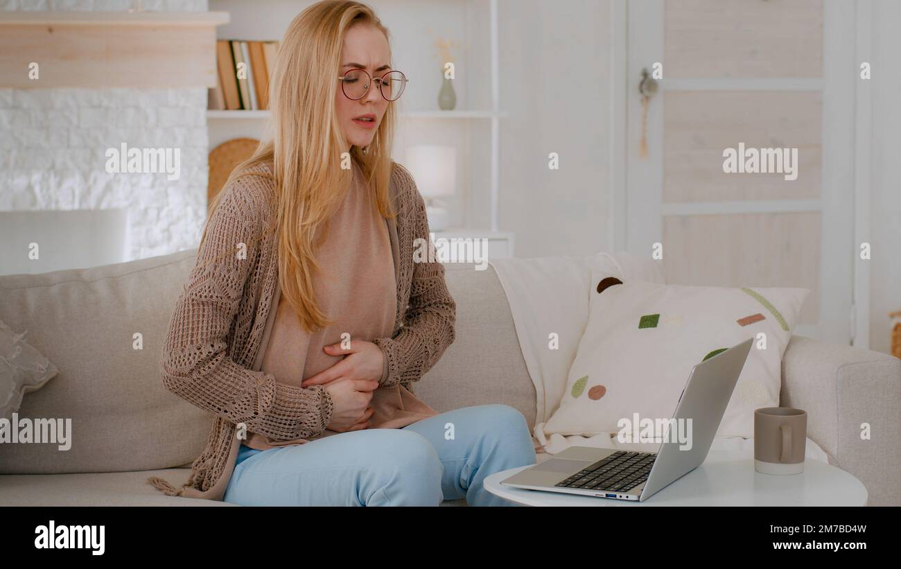 Malade fille étudiante femme d'affaires mal dame en lunettes maladie caucasienne femme avec ordinateur portable à la maison sensation de mauvais abdomen douleur ventre douleur souffrance Banque D'Images