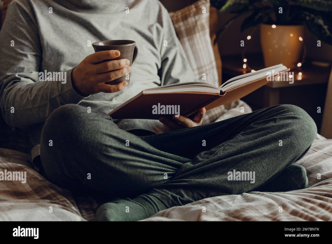 Un homme caucasien se reposant à la maison, lisant un livre, buvant du café au lit Banque D'Images