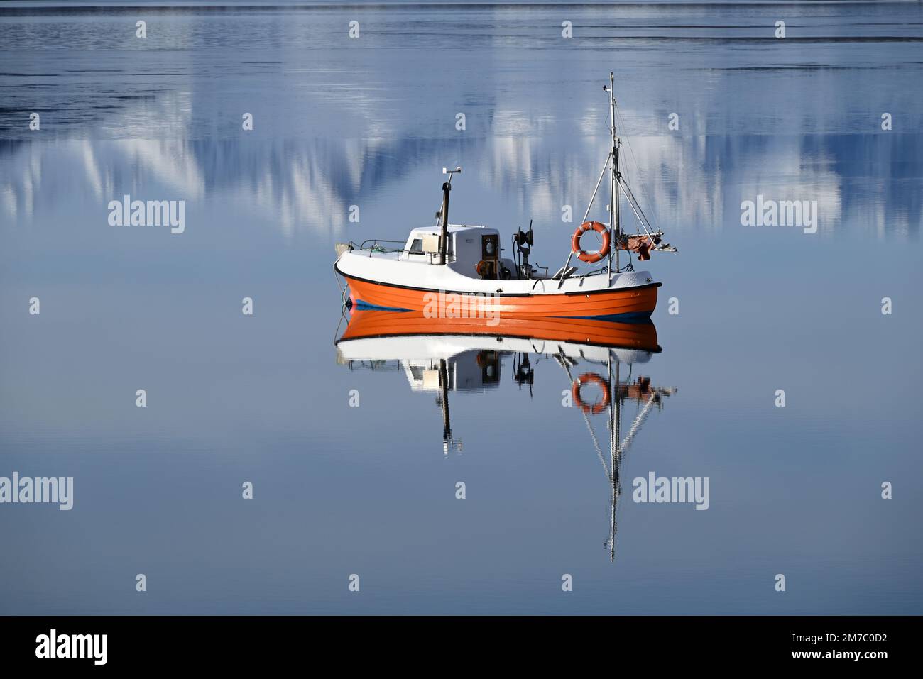 Un petit bateau de pêche ancré dans un fjord au sud d'Alta dans le nord de la Norvège tandis que les montagnes arrière se reflètent dans la mer. Banque D'Images