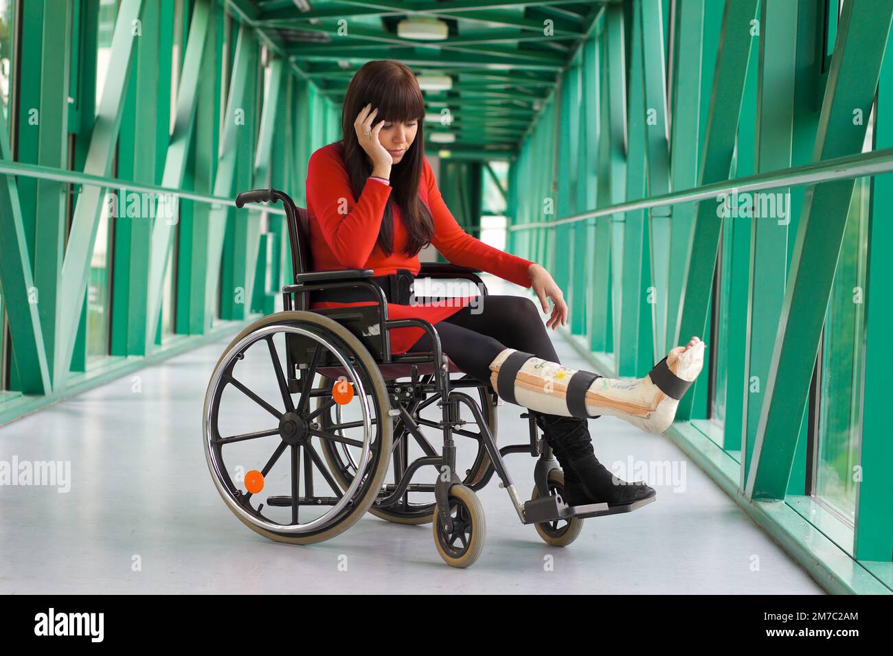 Femme frustrée assise avec une jambe courte dans un fauteuil roulant dans un couloir de l'hôpital, en Autriche Banque D'Images