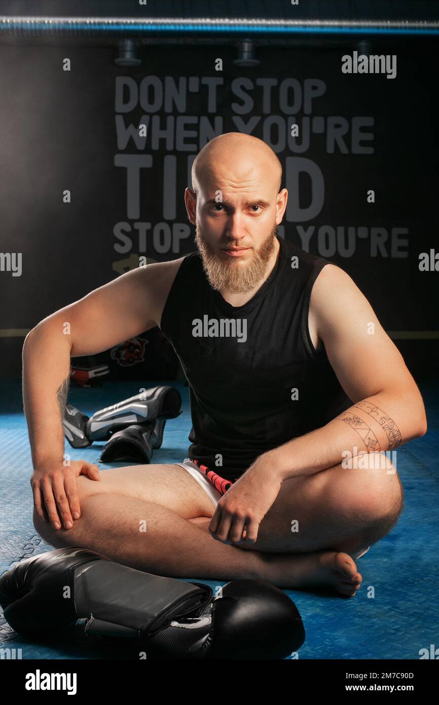 homme chauve avec barbe assis dans la salle de gym derrière des gants de boxe. regarder la caméra Banque D'Images