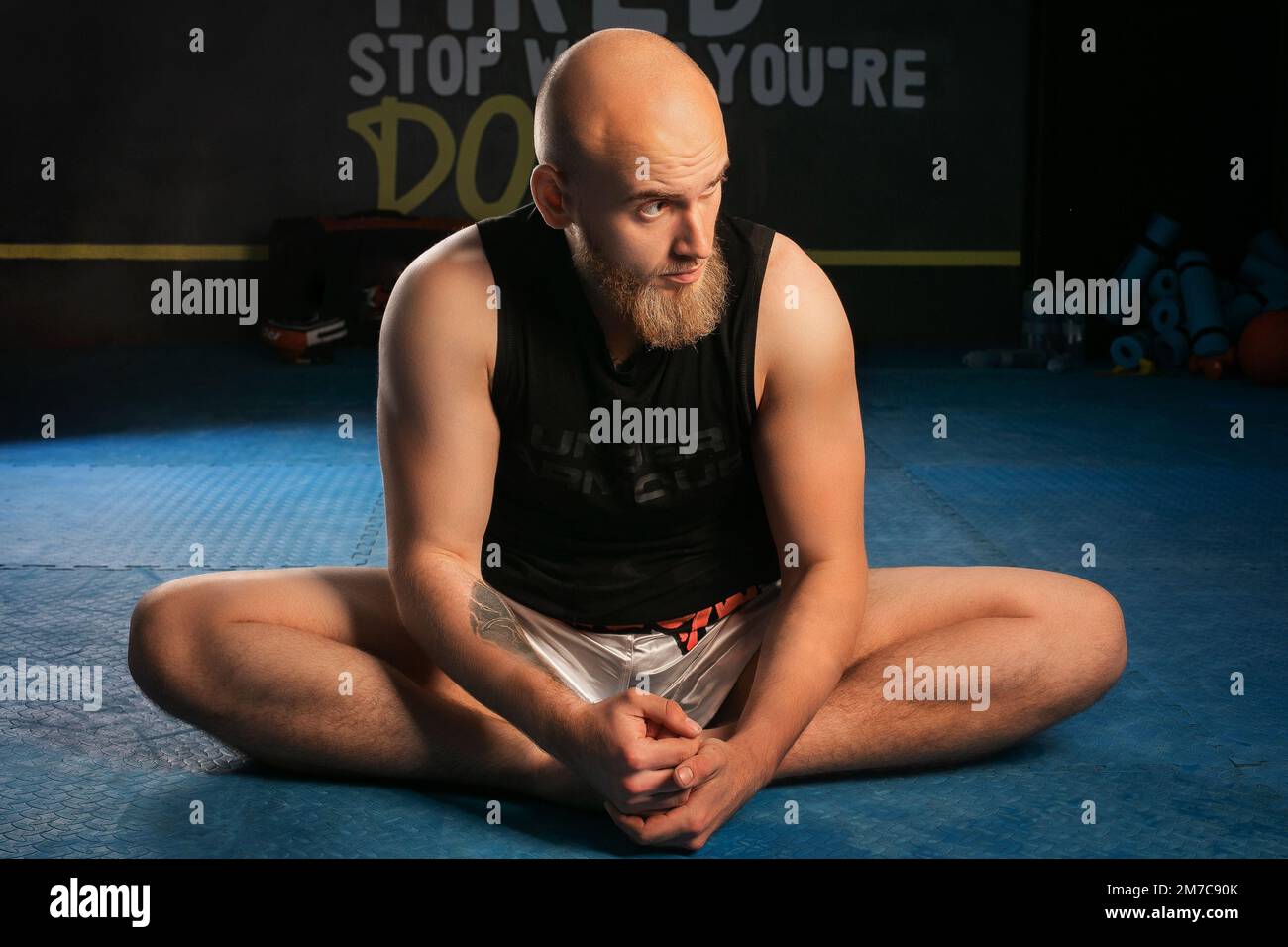 un homme chauve avec une barbe étire ses jambes avant l'entraînement. Banque D'Images