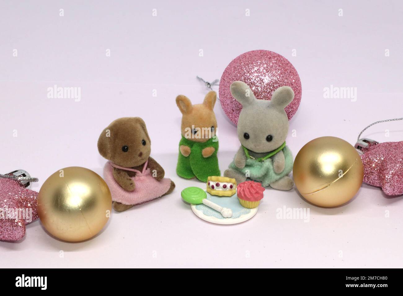 Un thème de Noël des animaux des familles Sylvanian assis autour de la nourriture de fête avec des boules autour d'eux. Décorations pour arbres de Noël dorées et roses scintillantes. Banque D'Images
