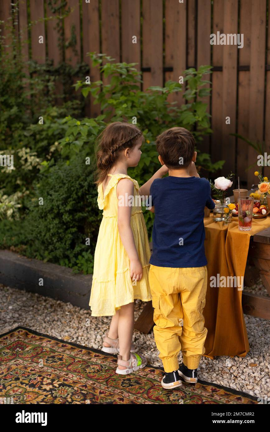 Enfants à la fête d'anniversaire, petite fille adorable et garçon avec boisson de limonade, en utilisant une paille, debout près de la table de fête d'anniversaire Banque D'Images