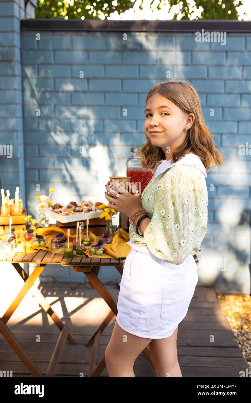 Portrait d'une petite fille buvant du jus dans un verre, décoré de fruits, avec de la paille dans le parc extérieur. Enfant en été Banque D'Images