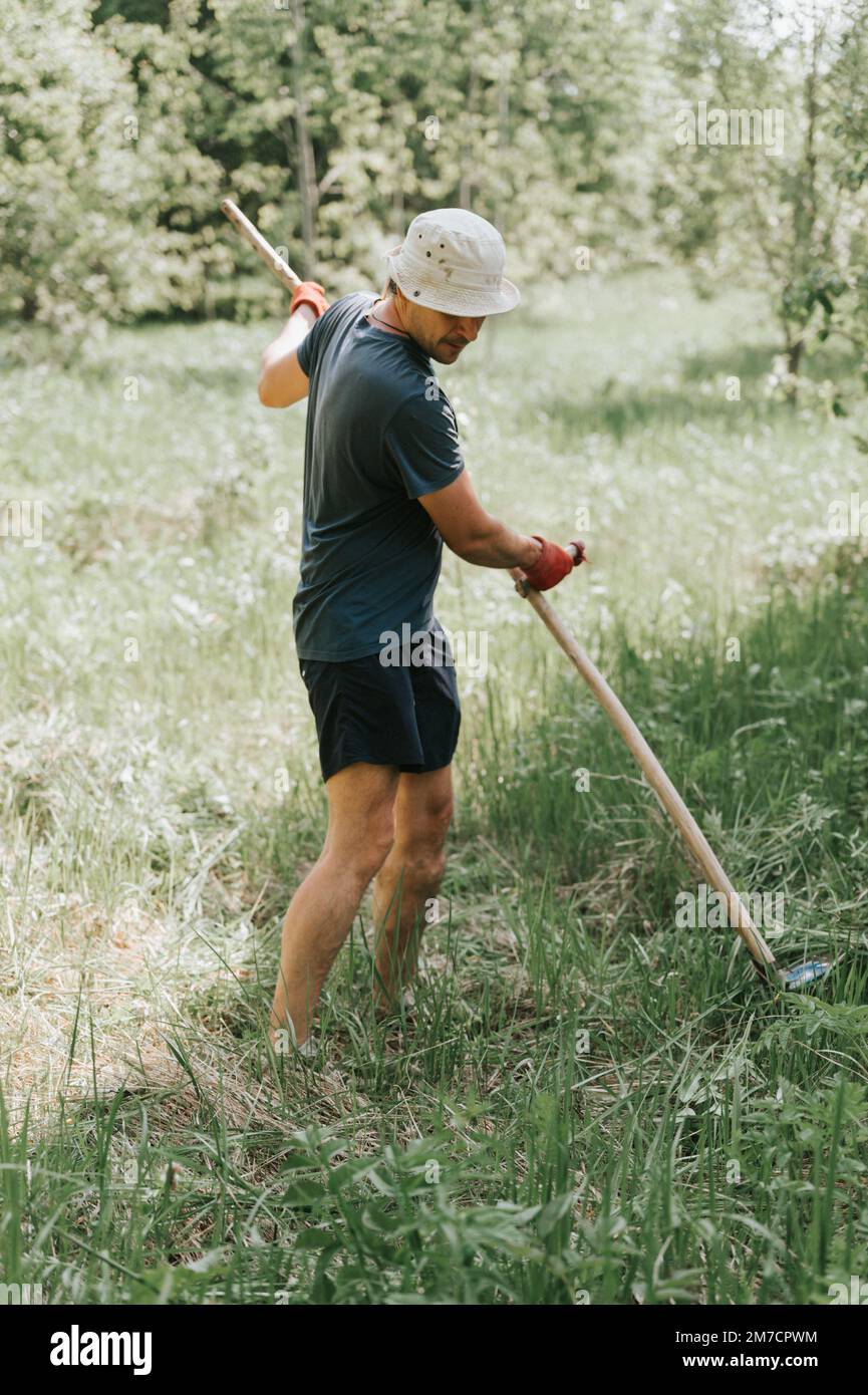 faucher l'herbe traditionnelle à l'ancienne avec la main scythe sur la ferme du village domestique. jeune agriculteur adulte fauchant le vert de l'herbe cultivée Banque D'Images