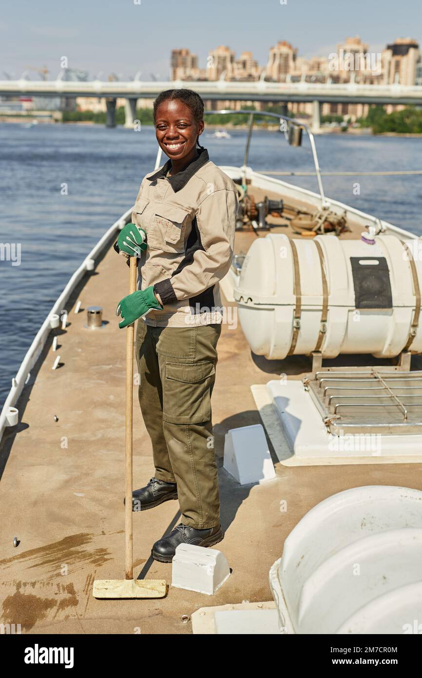 Portrait vertical de la femme souriante qui nettoie les sols du bateau ou du yacht à la lumière du soleil et regarde l'appareil photo Banque D'Images