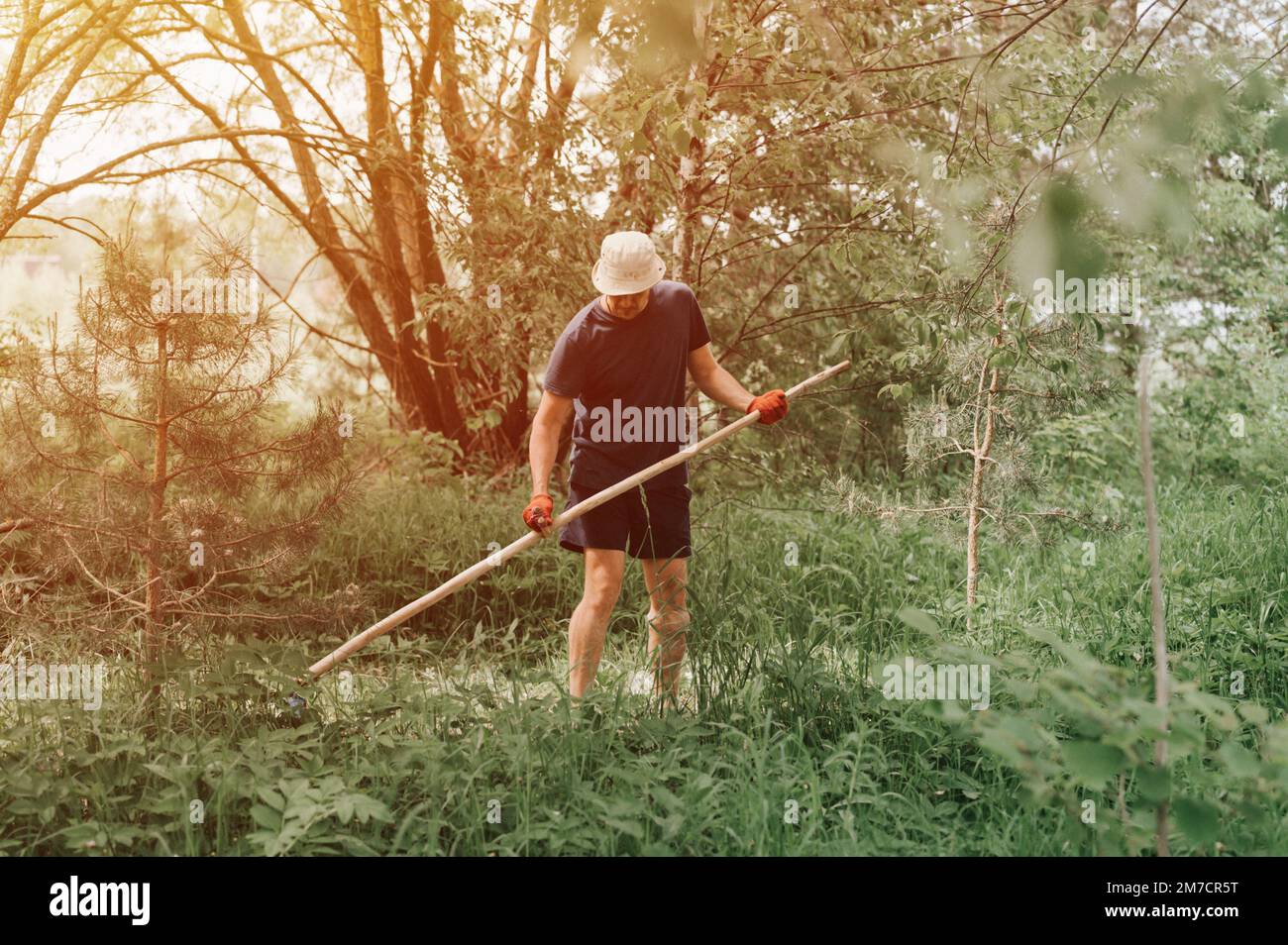 faucher l'herbe traditionnelle à l'ancienne avec la main scythe sur la ferme du village domestique. jeune agriculteur adulte fauchant le vert de l'herbe cultivée Banque D'Images