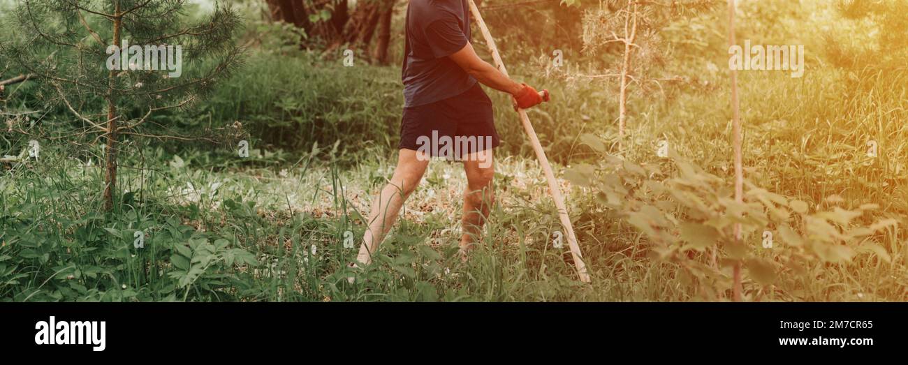 faucher l'herbe traditionnelle à l'ancienne avec la main scythe sur la ferme du village domestique. jeune agriculteur adulte fauchant le vert de l'herbe cultivée Banque D'Images