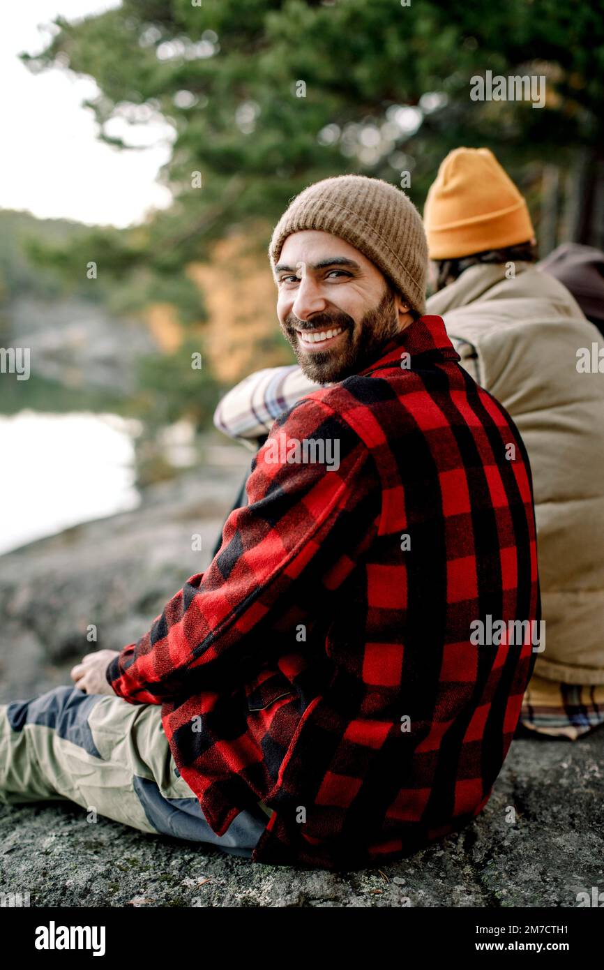 Un homme heureux portant une chemise à carreaux qui regarde par-dessus l'épaule tout en étant assis sur le rocher Banque D'Images