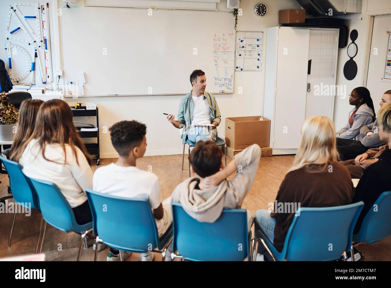 Professionnel de la santé mentale discutant avec des élèves de sexe masculin et féminin en thérapie de groupe à l'école Banque D'Images