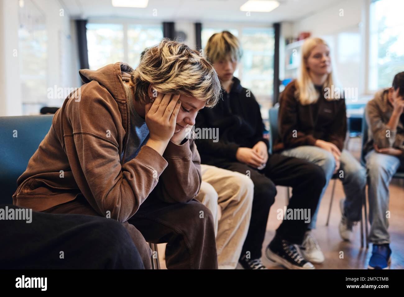 Une jeune fille adolescente triste avec la tête dans les mains, assise par des amis masculins et féminins en thérapie de groupe Banque D'Images