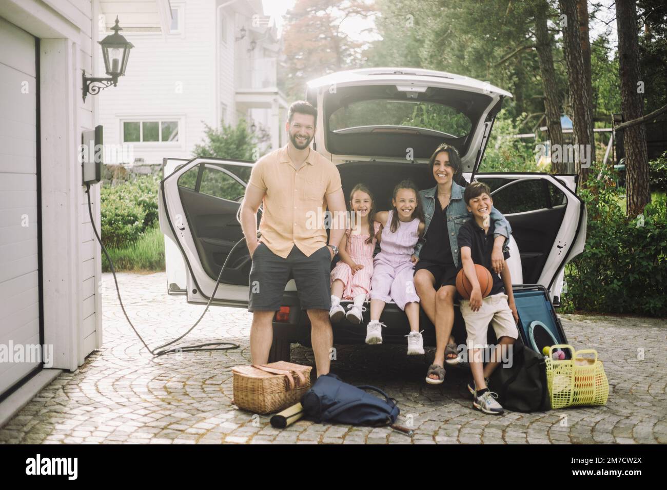 Portrait de famille heureuse assise dans le coffre électrique de voiture à l'extérieur de la maison Banque D'Images
