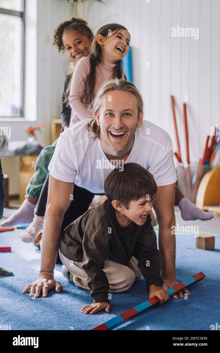 Joyeux préposé à la garde d'enfants appréciant avec des élèves de sexe masculin et féminin de la maternelle Banque D'Images
