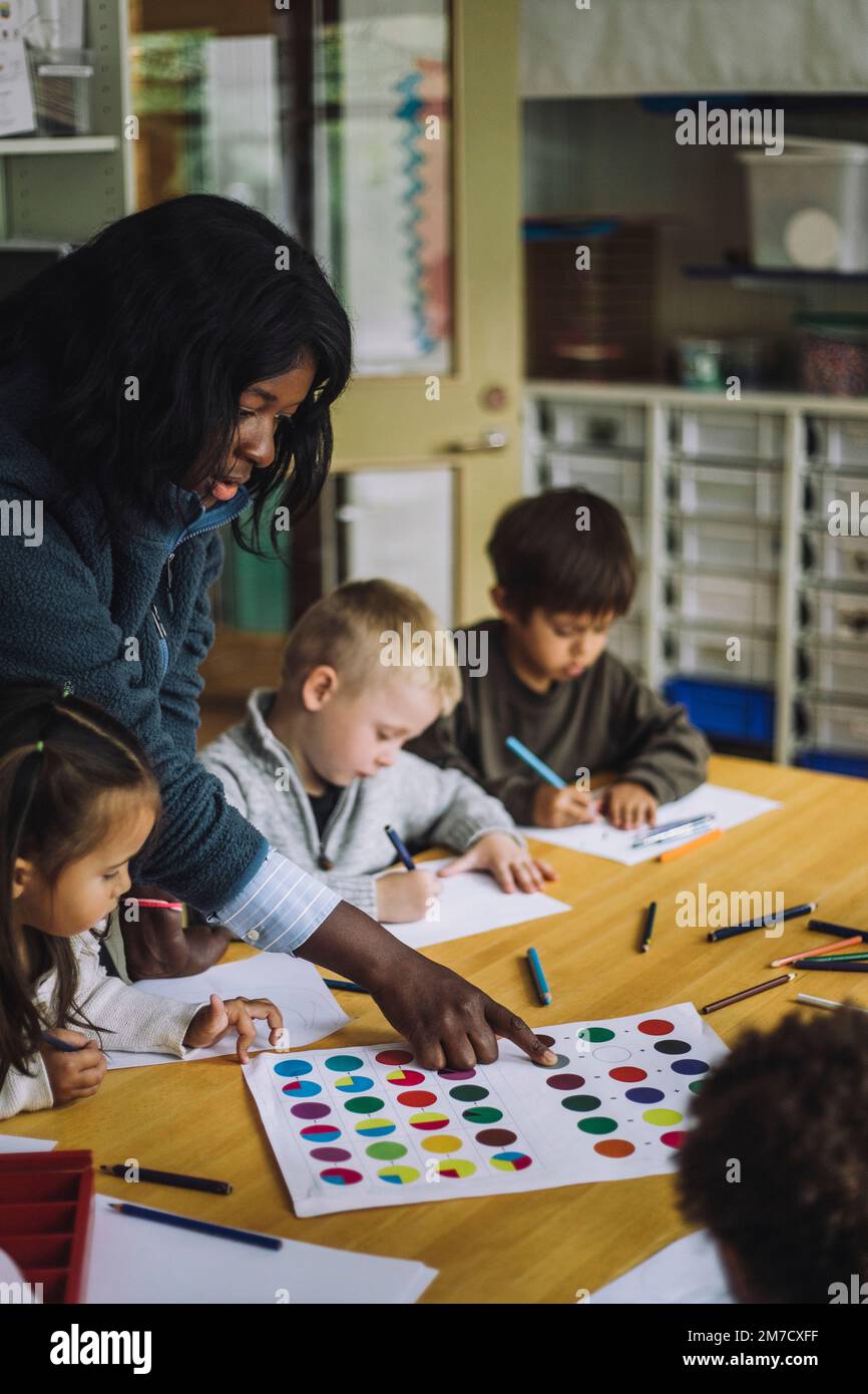 Une enseignante guide les élèves à reconnaître les couleurs tout en les formant dans un centre de garderie Banque D'Images