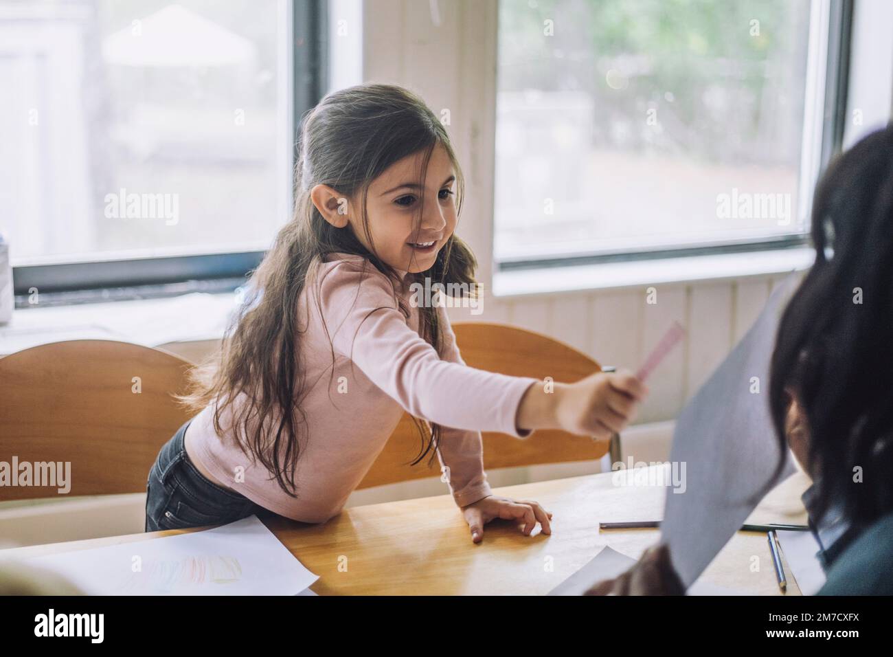 Fille souriante montrant le dessin d'un professeur pendant la classe d'art de la maternelle Banque D'Images