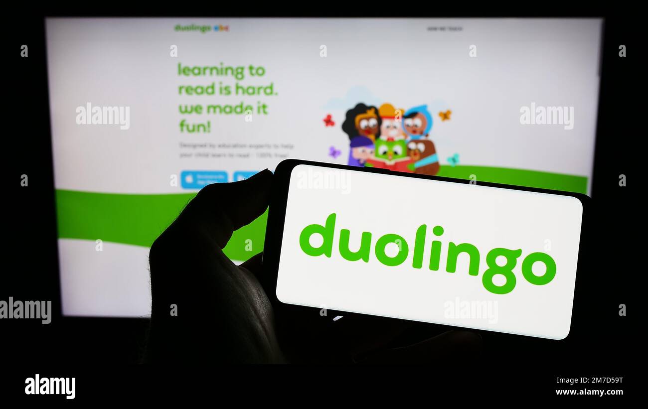 Personne tenant un téléphone cellulaire avec le logo de la société de technologie éducative Duolingo Inc. À l'écran devant la page Web. Mise au point sur l'affichage du téléphone. Banque D'Images