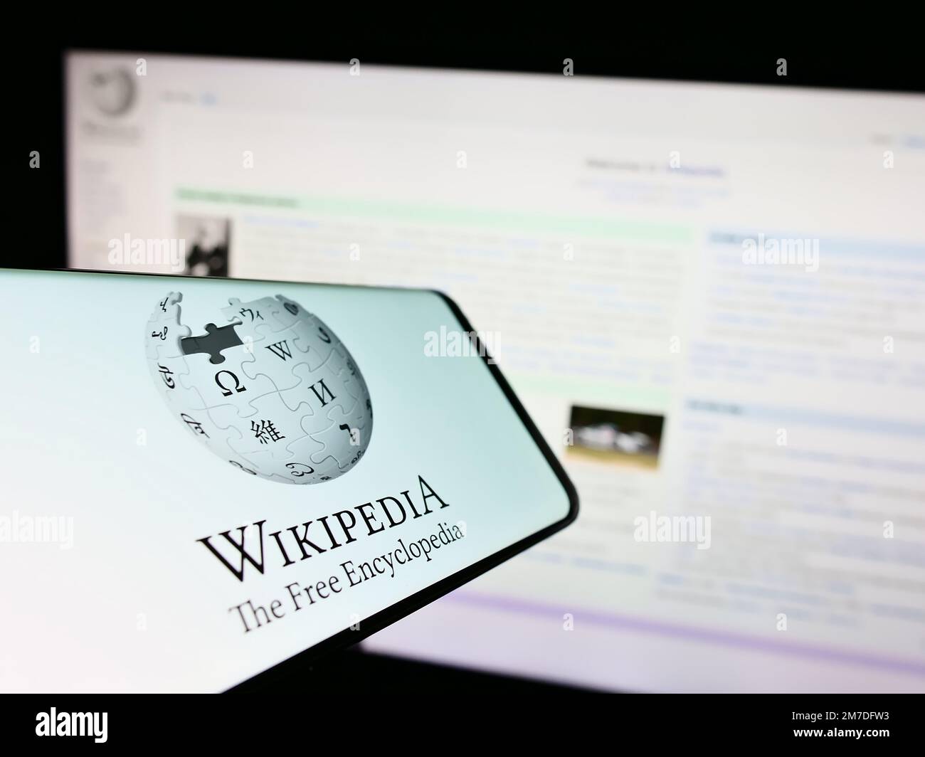 Smartphone avec logo de l'encyclopédie en ligne Wikipedia à l'écran en face du site Web. Effectuez la mise au point au centre-droit de l'écran du téléphone. Banque D'Images