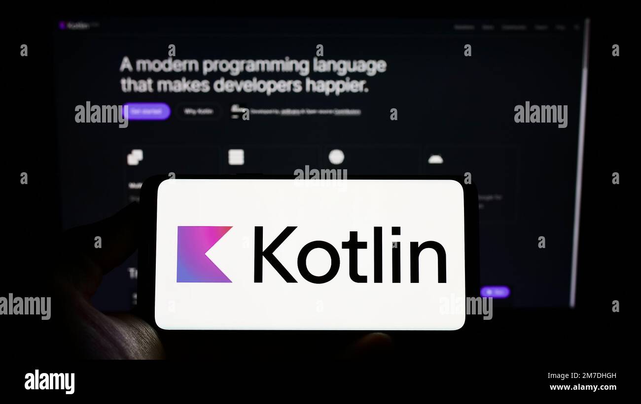 Personne tenant le téléphone portable avec logo de la langue de programmation Kotlin à l'écran en face de la page web. Mise au point sur l'affichage du téléphone. Banque D'Images