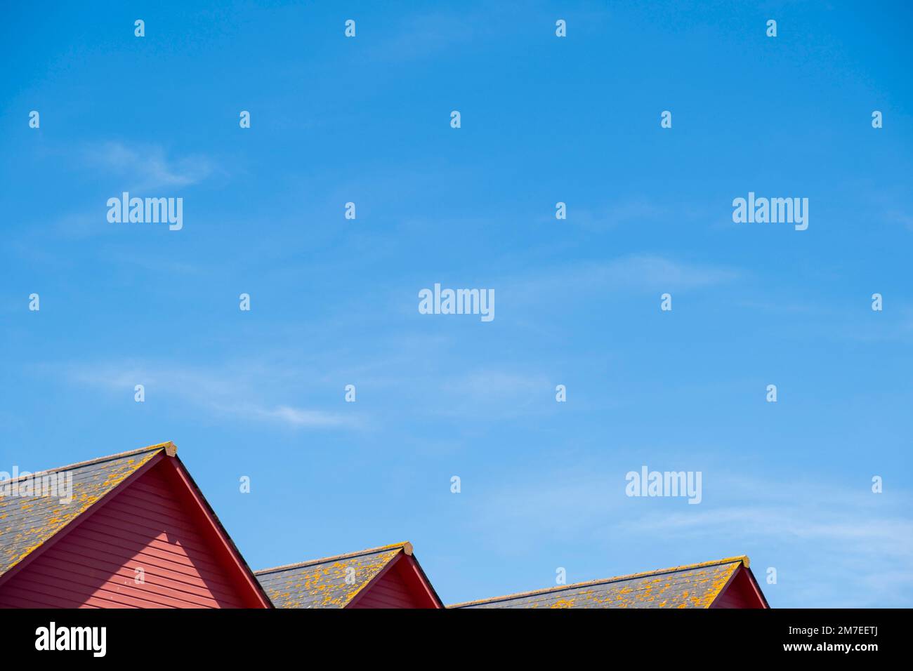 Vue sur une ligne de trois maisons au toit rouge et le ciel bleu avec des tuiles couvertes de lichen. Banque D'Images