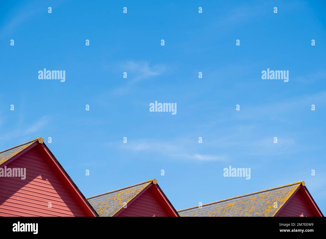 Vue sur une ligne de trois maisons au toit rouge et le ciel bleu avec des tuiles couvertes de lichen. Banque D'Images