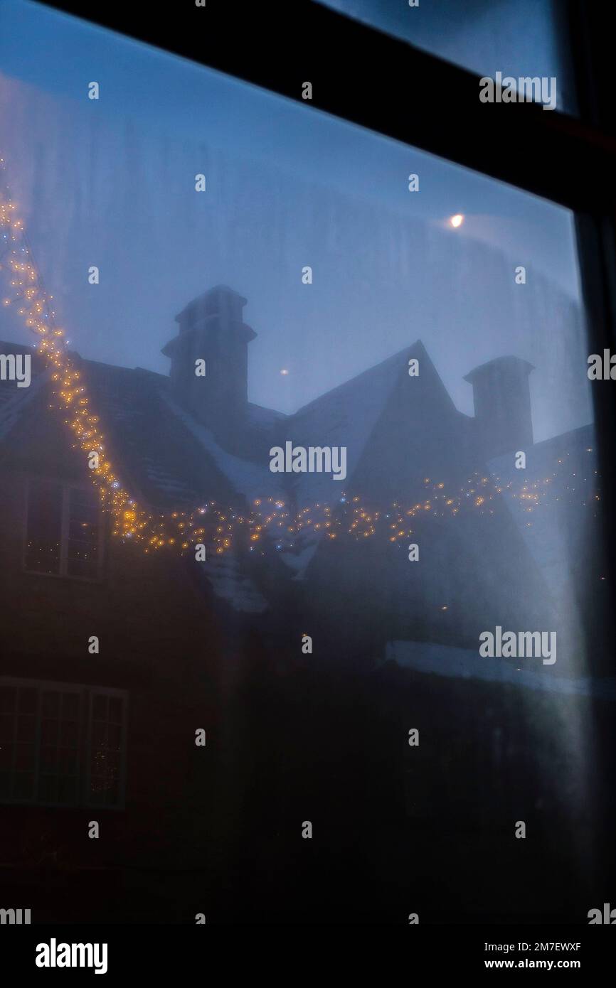 Vue à travers une fenêtre de café-restaurant sur la scène de rue nocturne dehors à Noël avec des lumières décoratives suspendues et gl;en étant dans la rue à l'extérieur. Banque D'Images