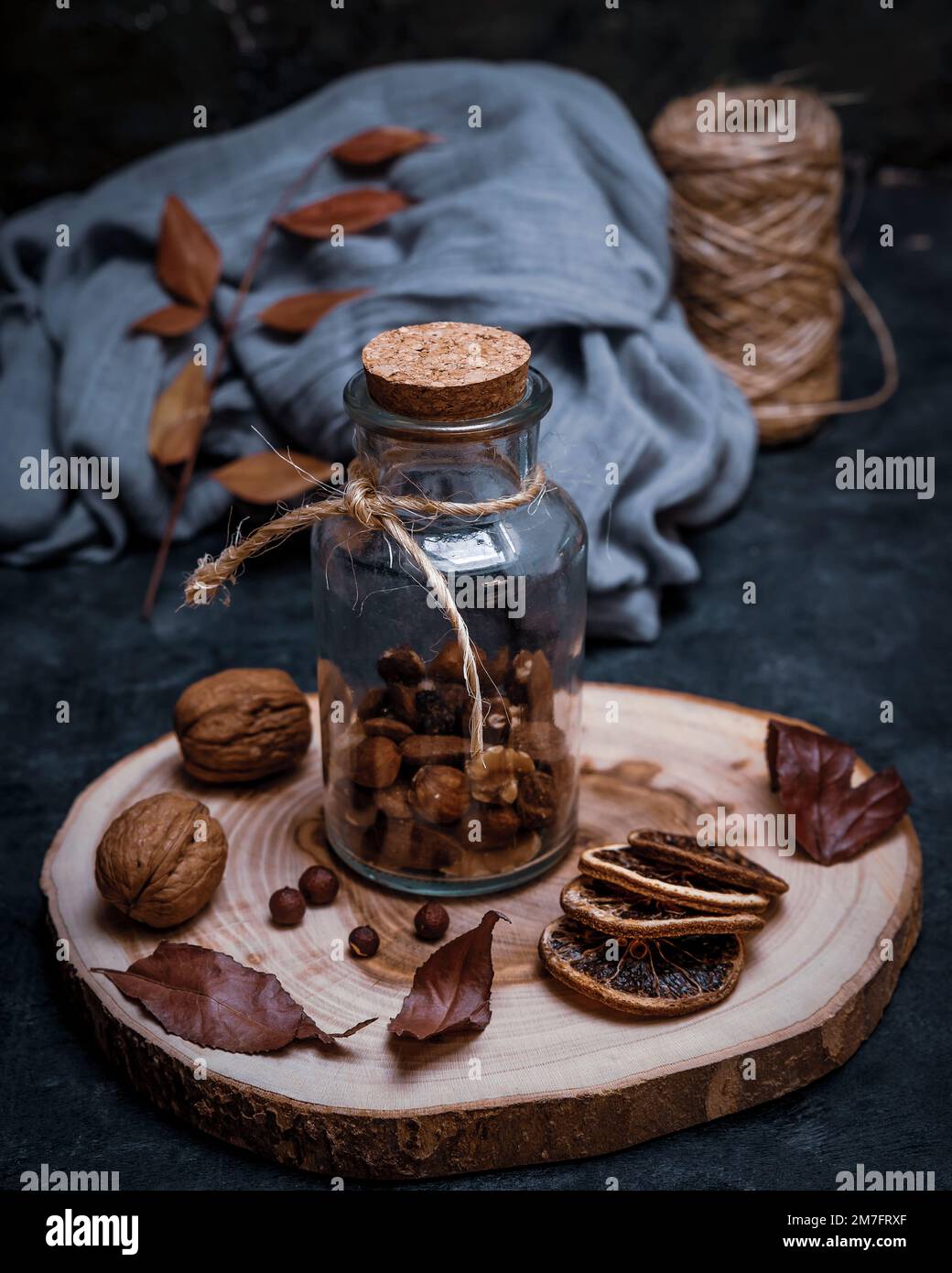 Récipient en verre avec fruits secs sur une planche à découper ronde en bois, avec noix et tranches d'orange séchées Banque D'Images