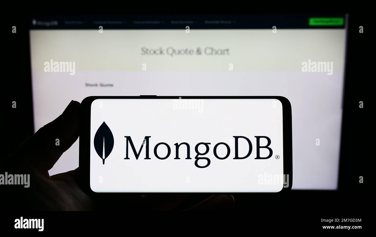 Personne tenant un téléphone mobile avec le logo de la société américaine de logiciels de base de données MongoDB Inc. À l'écran en face de la page Web. Mise au point sur l'affichage du téléphone. Banque D'Images