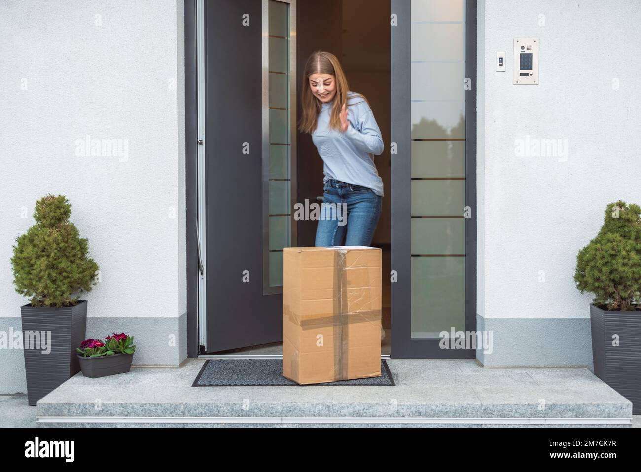 Jeune femme excitée ouvrant la porte d'entrée et voyant le paquet sur le tapis de porte Banque D'Images