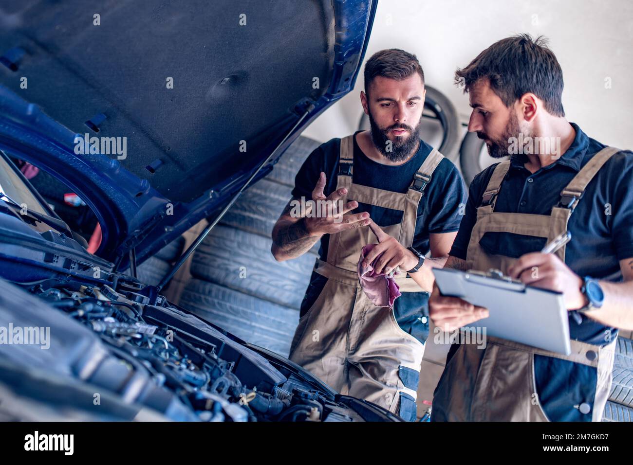 Jeunes mécaniciens automobiles qui changent l'huile lors de la réparation du moteur d'une voiture dans un atelier. Banque D'Images