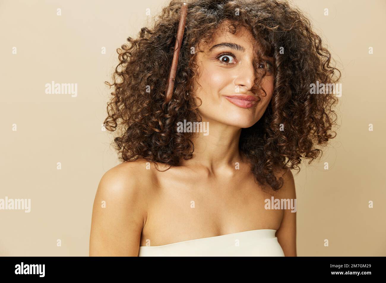 Femme peigne les cheveux bouclés afro avec peigne en bois, produits de coiffage de soins de beauté maison, perte de cheveux après Covid-19, sourire sur fond beige Banque D'Images