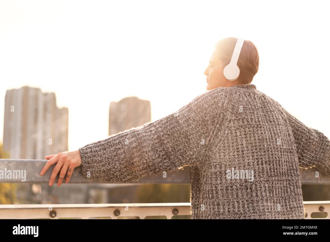 Jeune femme élégante aux cheveux courts avec casque sur le pont qui regarde la ville au coucher du soleil. Banque D'Images