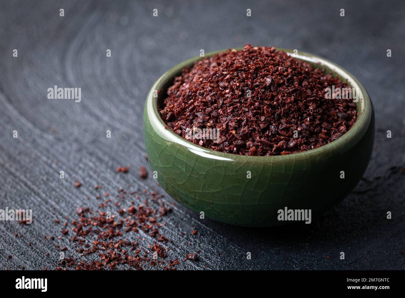 Poudre de Sumac rouge moulu séchée dans un bol vert sur fond sombre. Banque D'Images