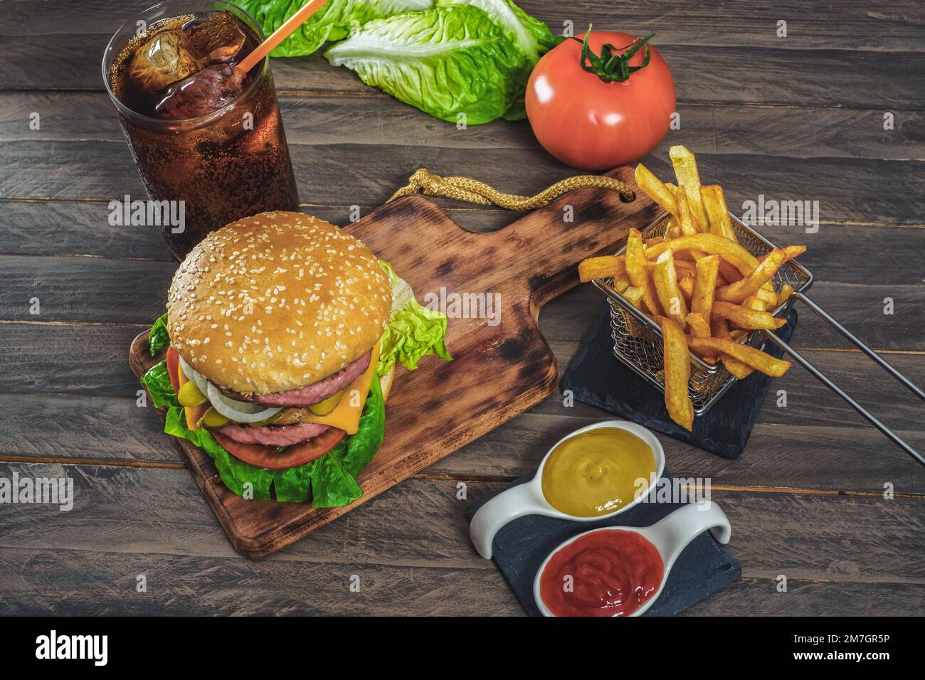 Hamburger complet avec deux viandes, sauces, frites et cola sur un panneau en bois antique Banque D'Images