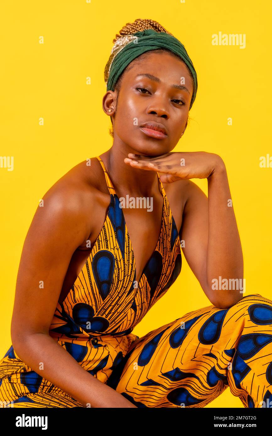 Jeune femme africaine avec costume traditionnel sur fond jaune, assis regardant la caméra Banque D'Images
