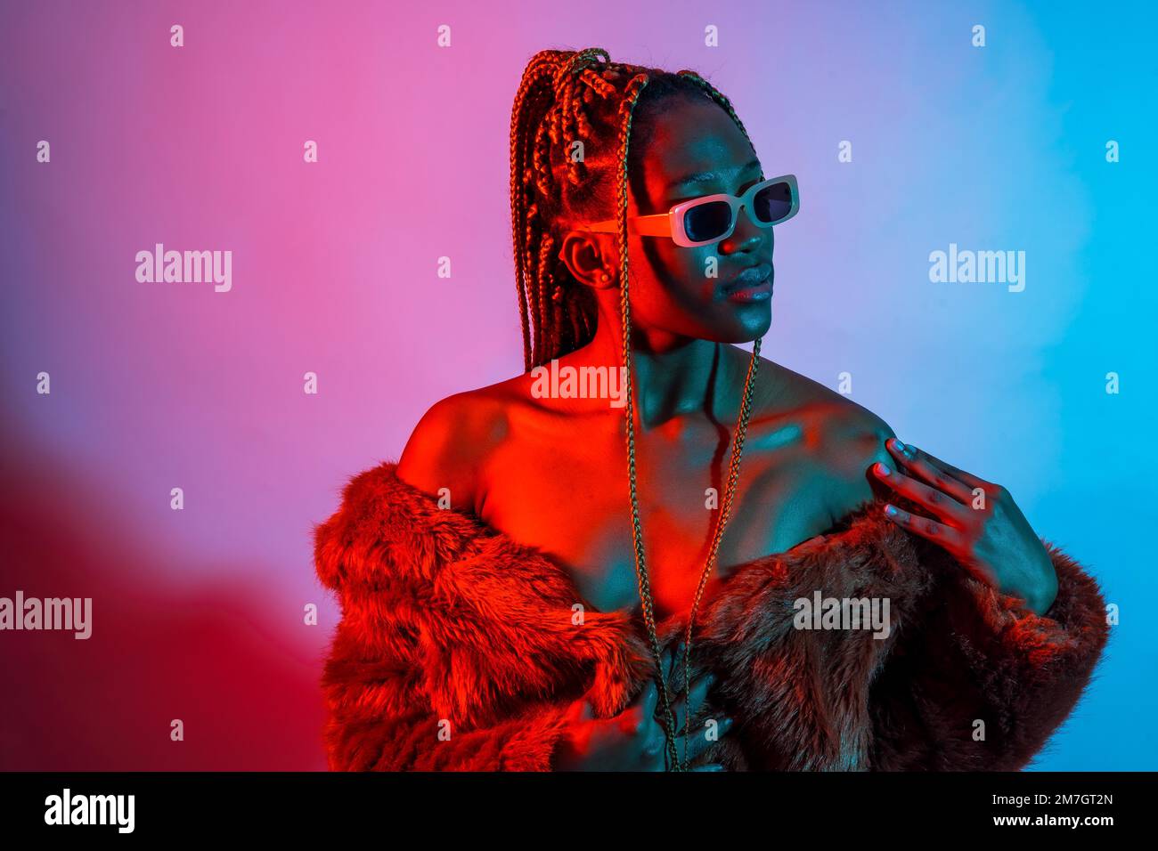Belle femme ethnique noire avec des tresses avec des lumières à DEL rouges et bleues, studio de tournage urbain Banque D'Images