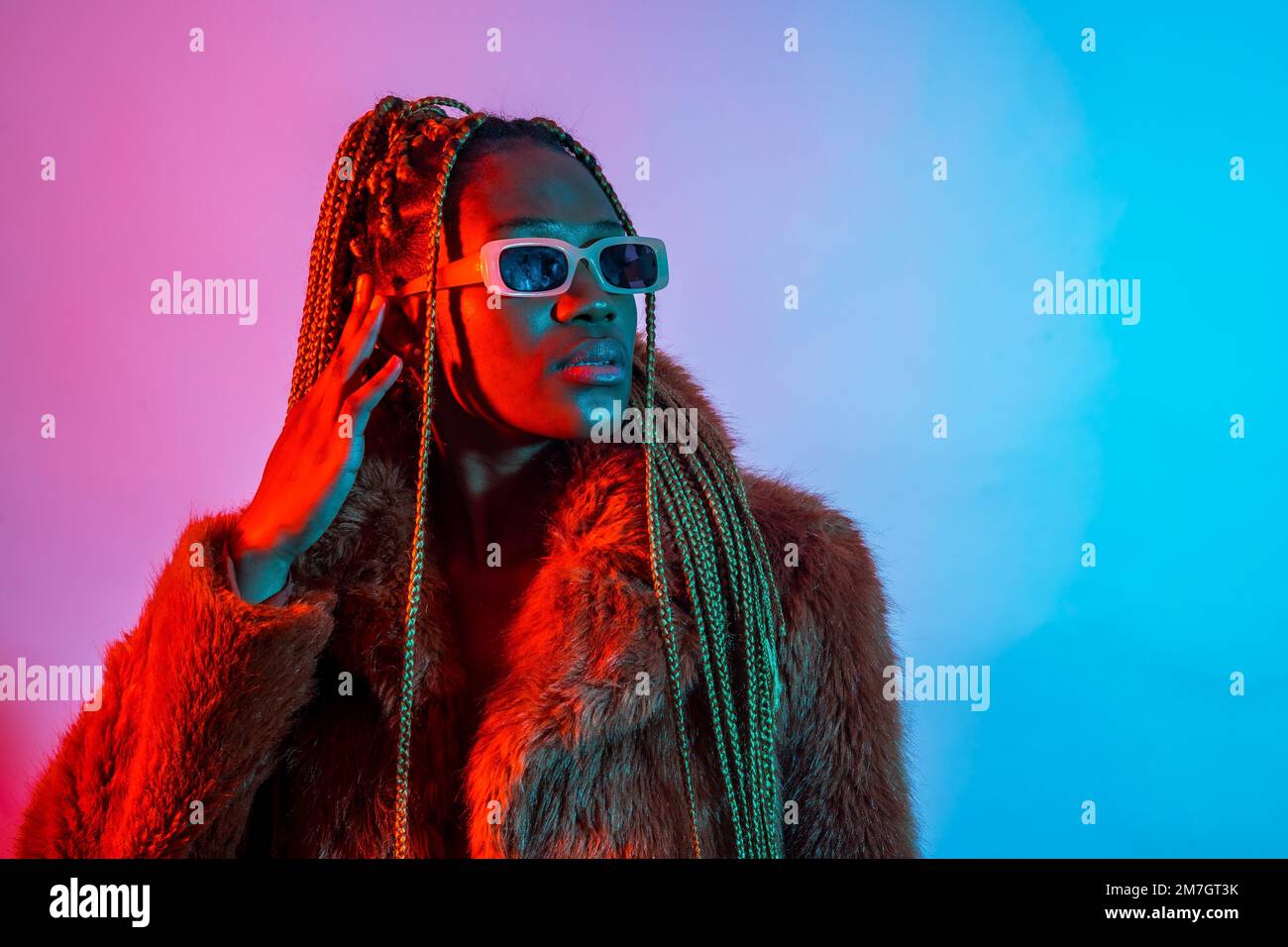 Femme ethnique noire avec des tresses avec des lumières à DEL rouges et bleues, studio de tir avec des lunettes de soleil Banque D'Images