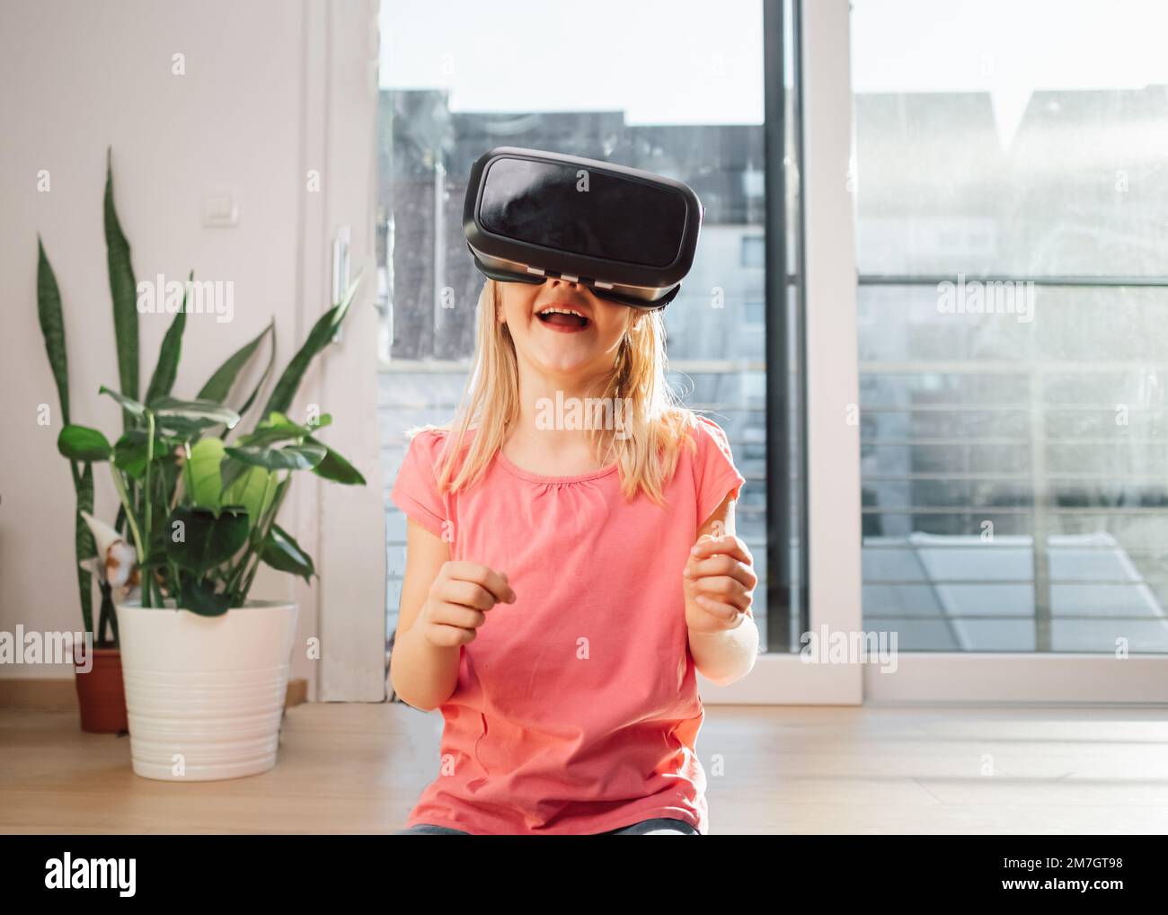 Blonde gaie enfant souriant et appréciant dans le monde de la réalité virtuelle à l'aide de lunettes VR. Enfants, technologie et développement. Banque D'Images