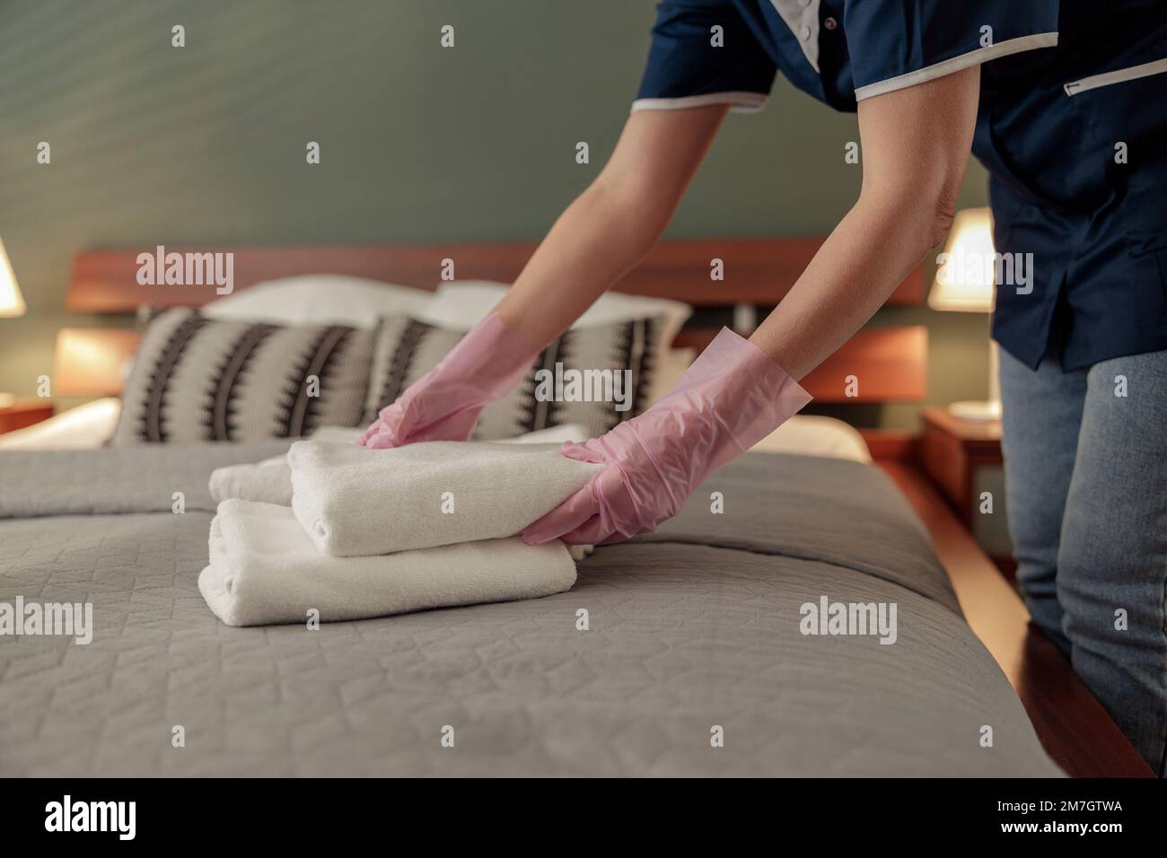 Gros plan des mains de la femme de ménage mettant une pile de serviettes de bain blanches fraîches sur le drap de lit. Concept de service d'étage Banque D'Images