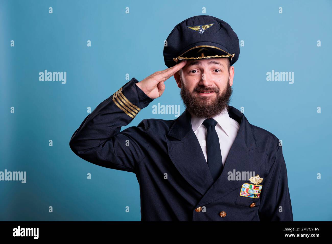 Souriant capitaine d'avion saluant, portant un uniforme d'aviation et un chapeau vue de face portrait, capitaine d'avion regardant la caméra. Pilote de l'Aviation academy avec badge des ailes de la compagnie aérienne sur la veste Banque D'Images