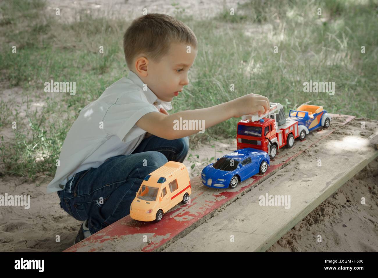 Un petit garçon joue avec des voitures jouets sur une aire de jeux extérieure Banque D'Images