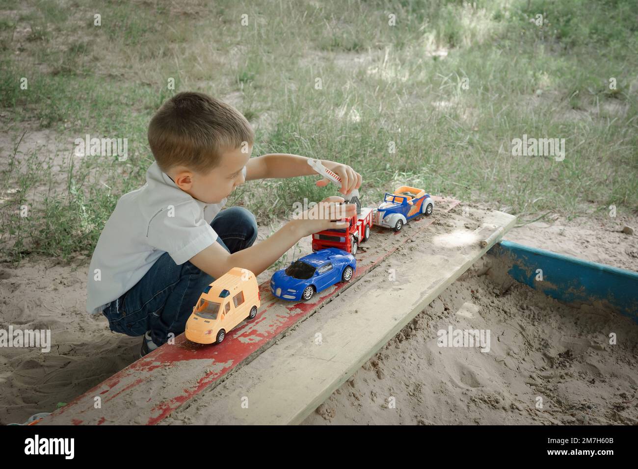 Un petit garçon joue avec des voitures jouets dans le bac à sable en plein air Banque D'Images