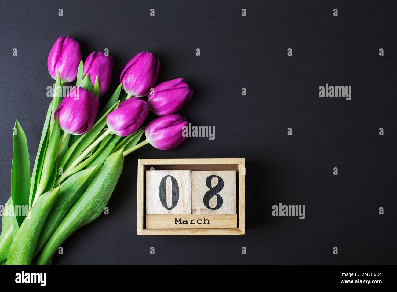 Bouquet de tulipes violettes et calendrier en bloc de bois avec date du 8 mars sur table noire. Concept des fêtes de jour pour femme. Vue de dessus, plan d'agencement, espace de copie. Banque D'Images