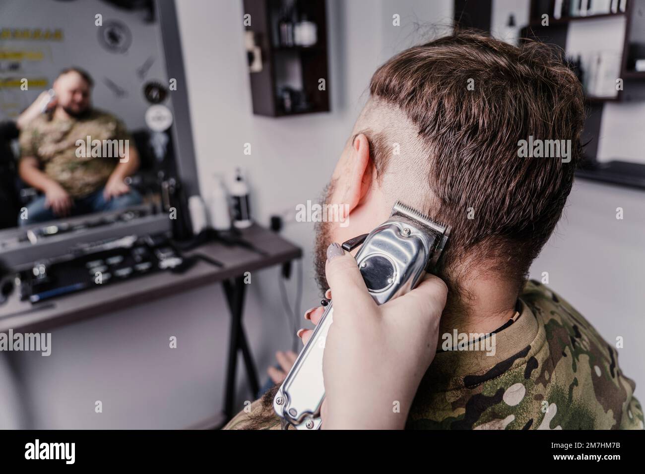 Un jeune homme dans un uniforme militaire se prépare à la tête chauve pour le service militaire. Un gars avec une barbe obtient une coupe de cheveux dans un salon de coiffure. Rasez votre tête chauve Banque D'Images
