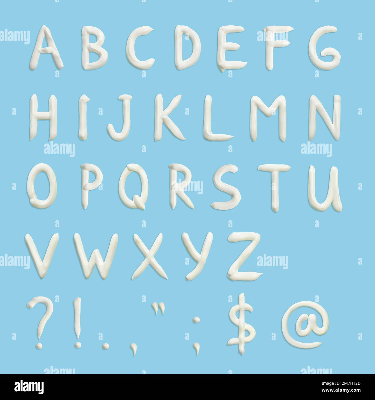 Lettres de l'alphabet anglais, signes de ponctuation et divers symboles sous forme de crème pressée en blanc sur fond bleu. Banque D'Images