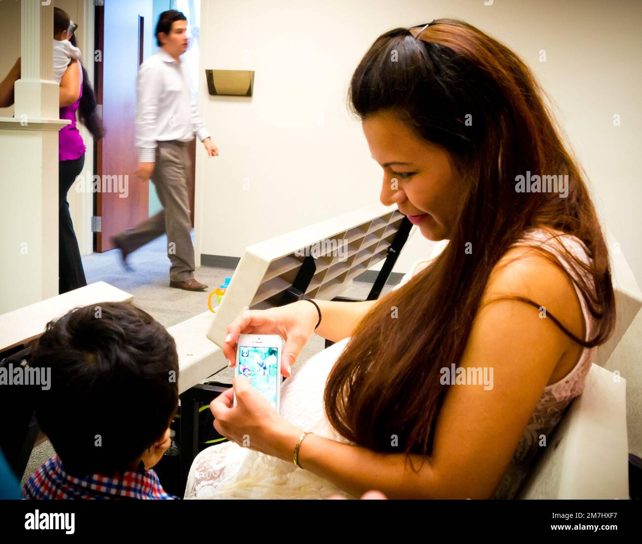 Femme mexicaine qui est enceinte à son service de mariage, assise avec un enfant qui est à côté d'elle, tenant un téléphone Banque D'Images