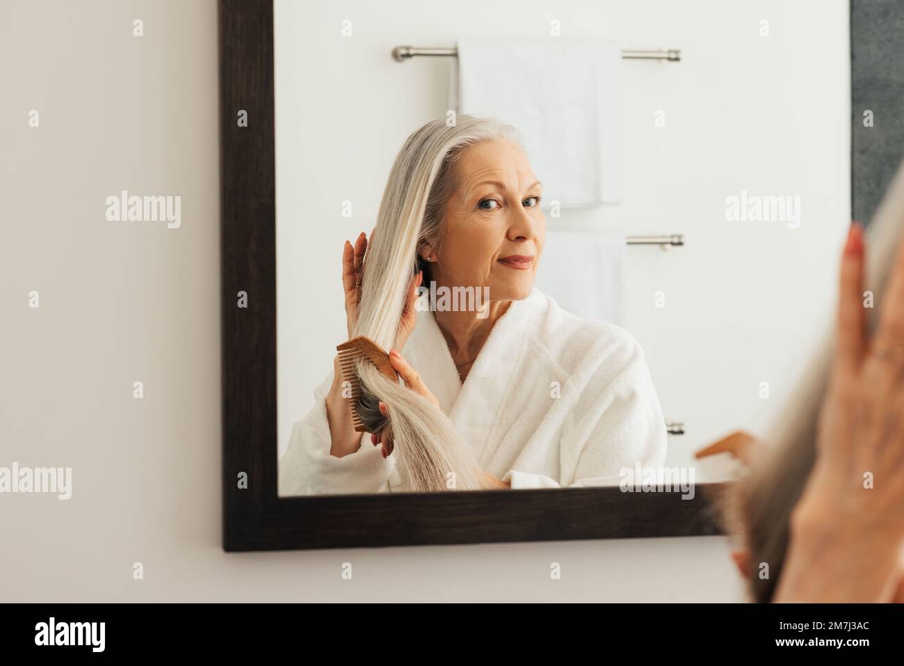 Femme âgée regardant le miroir tout en peignant ses cheveux longs dans la salle de bains Banque D'Images